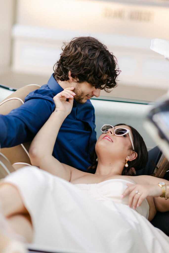 Aaron leaning over to kiss Kenia in the front seat of vintage car
