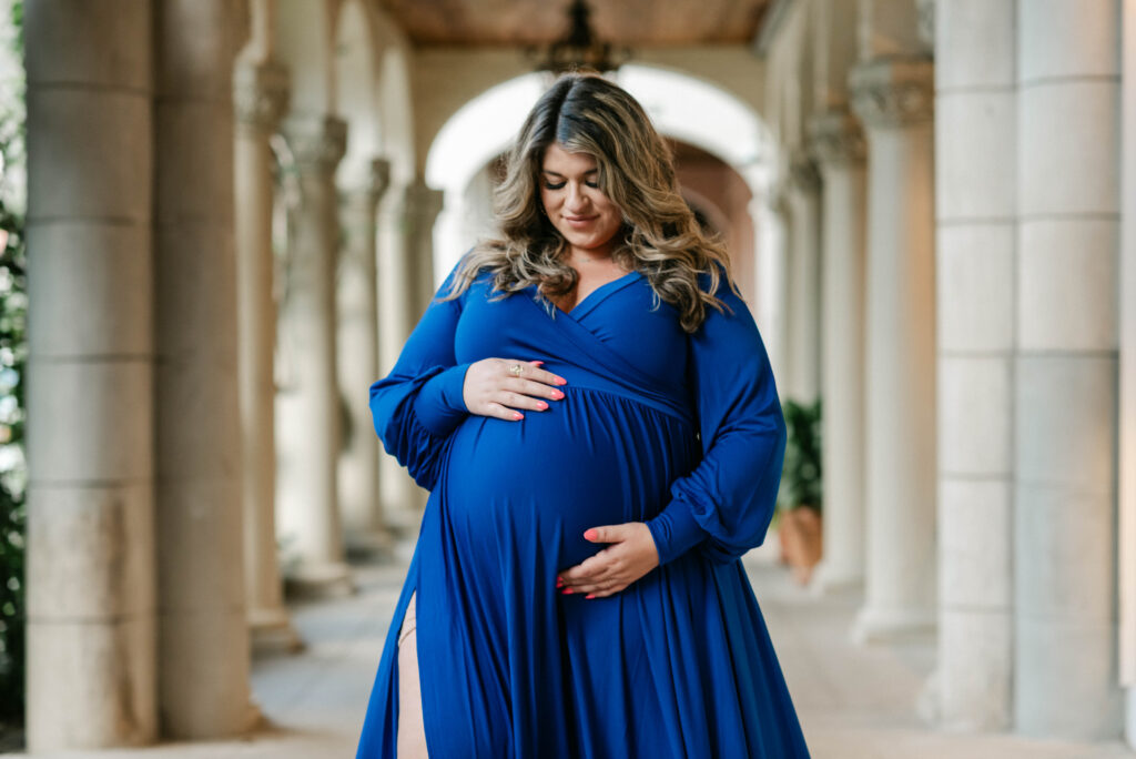 Pregnant woman holding baby bump in front of historic arch on Worth Avenue