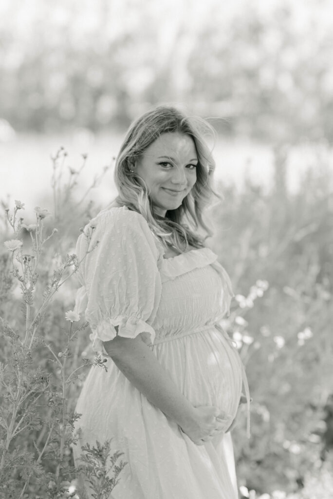 Expecting parents standing in a field at Kai-Kai Farm with soft morning light and greenery