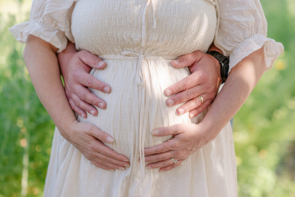 Close-up of hands over baby bump during a summer maternity session at Kai-Kai Farm