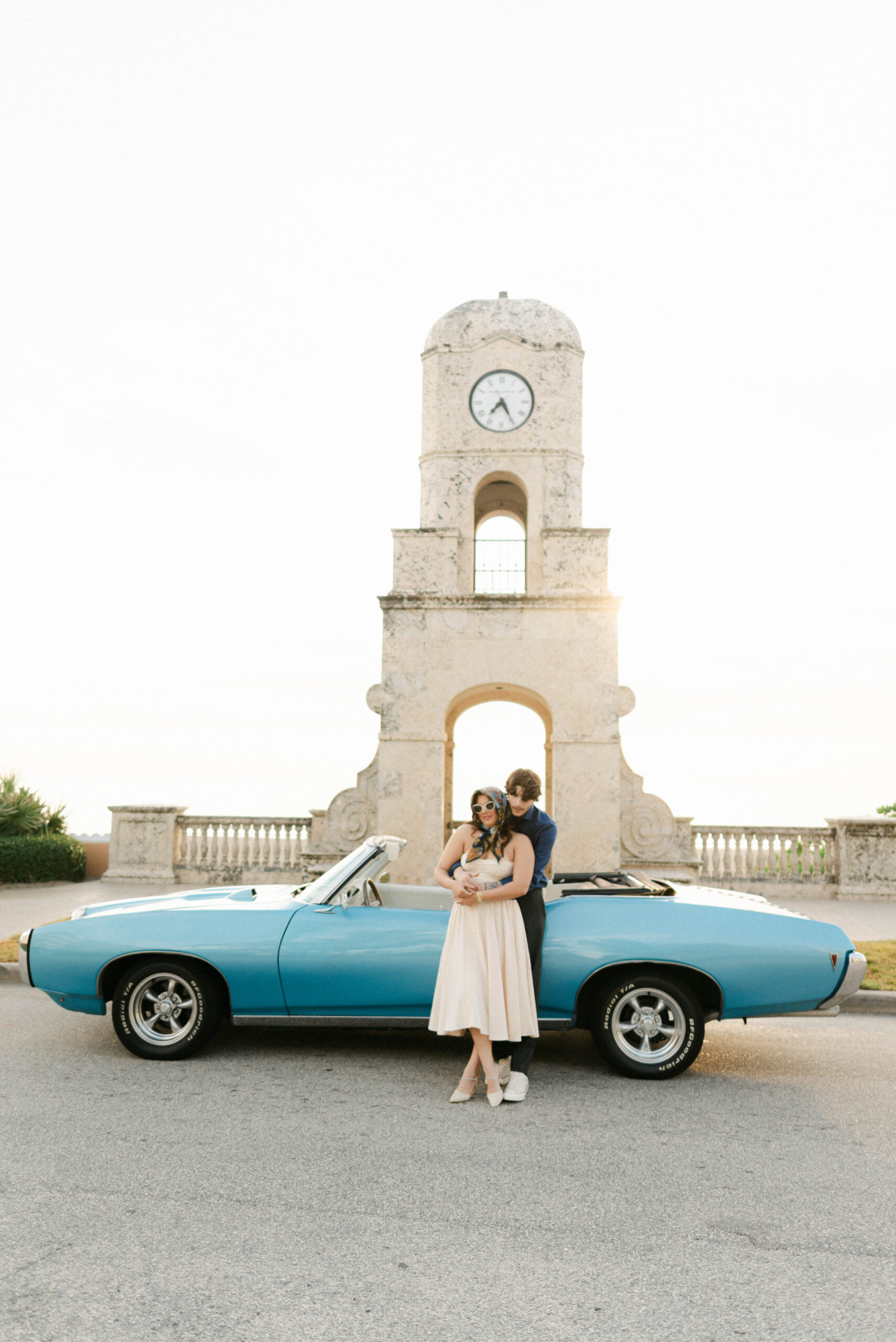 couple leans against vintage convertible with soft sunlight behind them on worth avenue