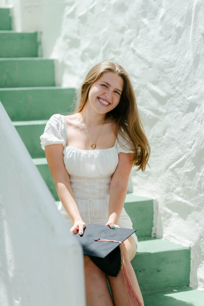 Emma sitting on green steps in white mini dress during Palm Beach photo shoot