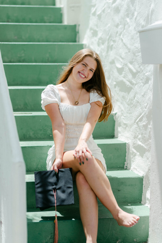 Graduate posing on green stairs at Worth Avenue in white mini dress