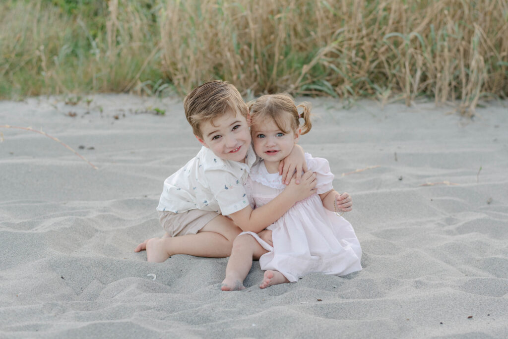 brother and sister smiling in neutral tones during family session