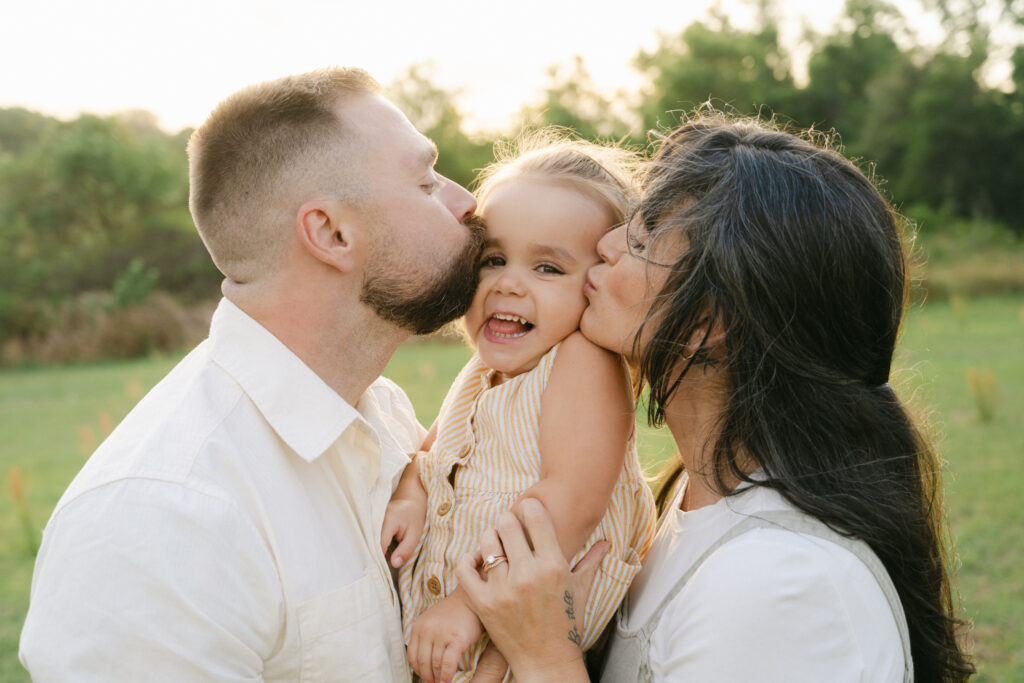 mom and dad kissing baby girl who is laughing at an ocala family session