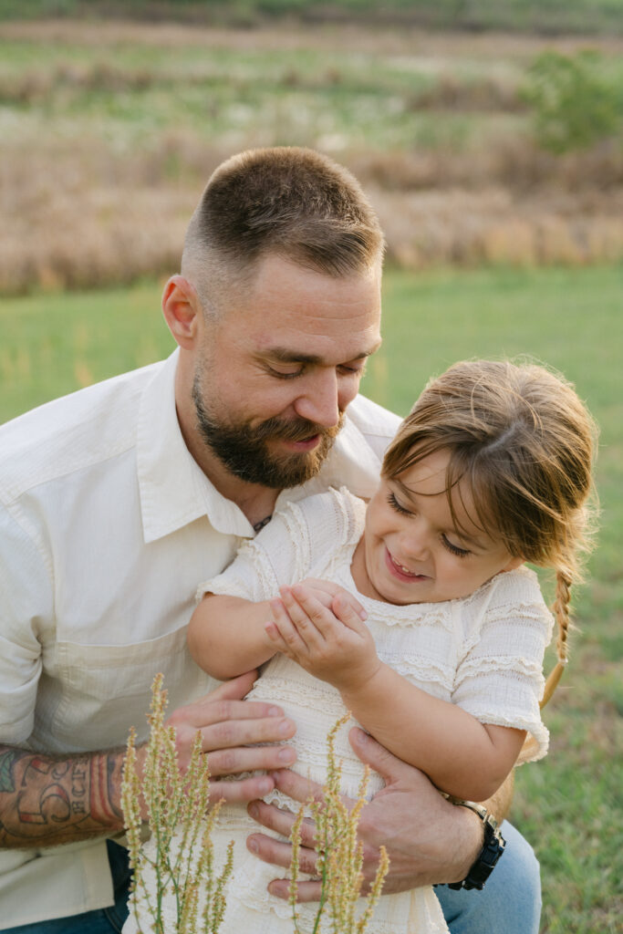 father tenderly holding smiling daughter in a grassy ocala field